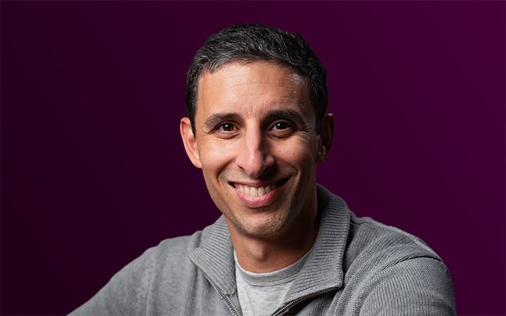 Smiling gray-haired person on a purple background.