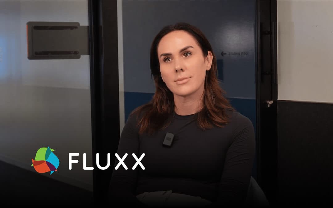 Seated person with shoulder-length brown hair wearing a black shirt, with “FLUXX” text below.