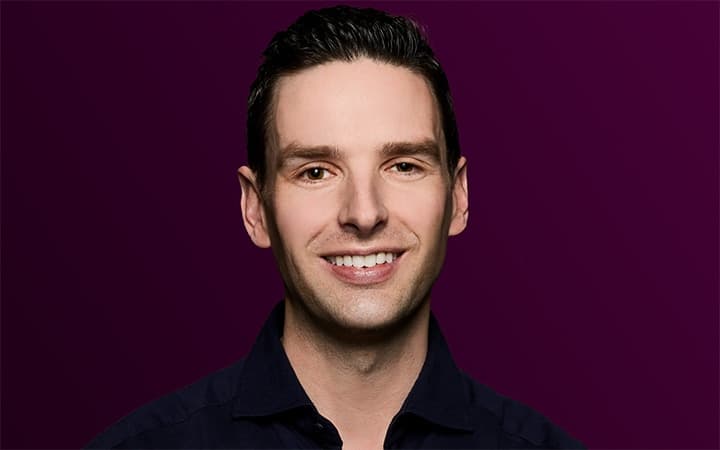 Smiling person in a dark shirt on purple.