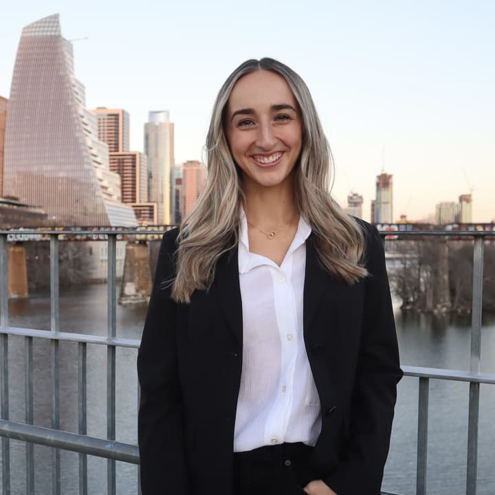 Smiling person in a black suit by a city waterfront