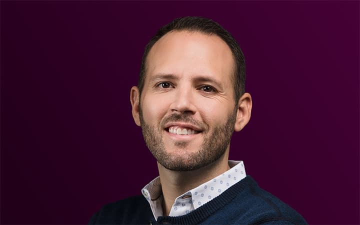 Smiling bearded person on a purple background.