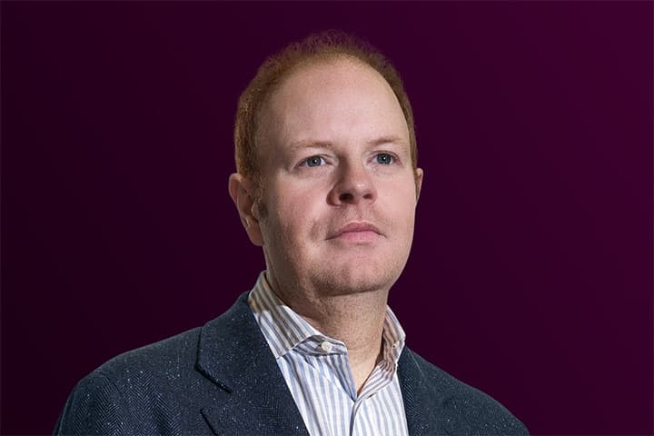 Fair-haired person wearing a blazer on purple.