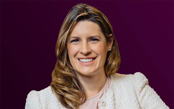 Smiling person with blond hair on a purple background.