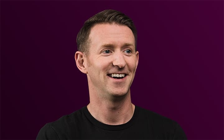 Smiling person in a black shirt on purple.