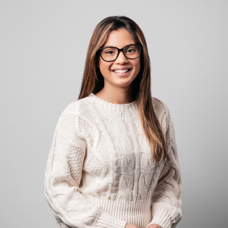 Smiling person with glasses wearing a white sweater.