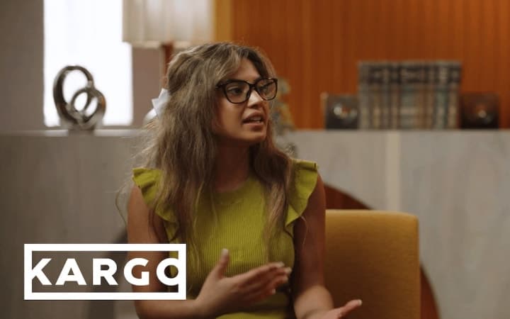 Person with glasses speaking in a chair, with “KARGO” text.